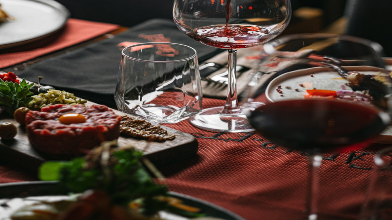 A wine bottle, mid wine-pour, at a steakhouse-style restaurant table.