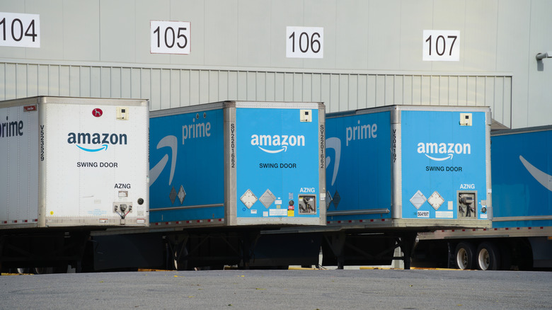 A row of Amazon trucks sit at loading docks at an Amazon fulfillment center