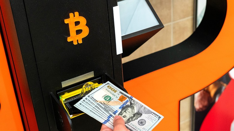 Person's hand seen inserting cash into a bitcoin ATM