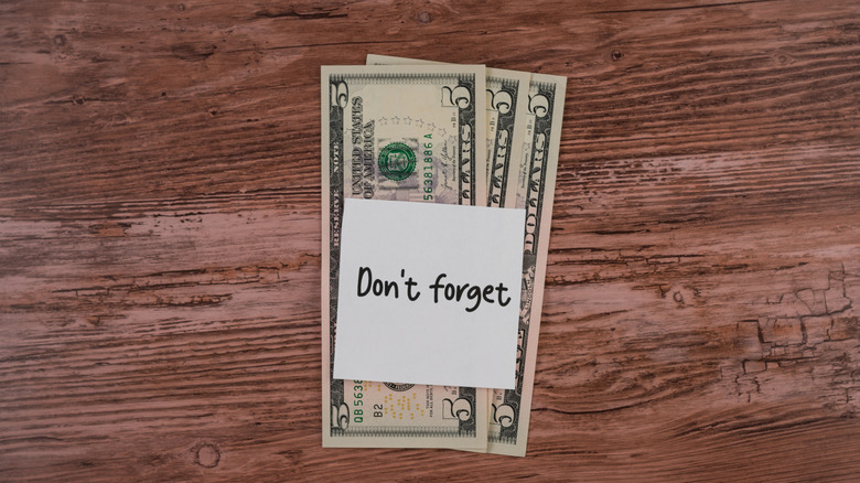 Three five-dollar bills laid out on a wooden tabletop with a sticky note that reads: 