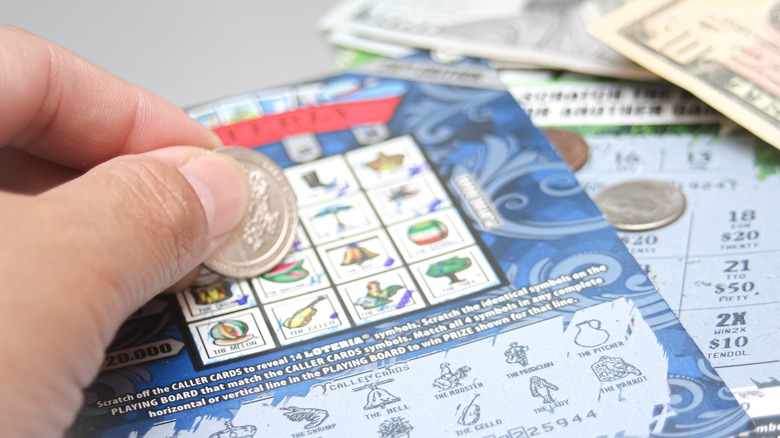 A hand using a coin to scratch off a lottery ticket.