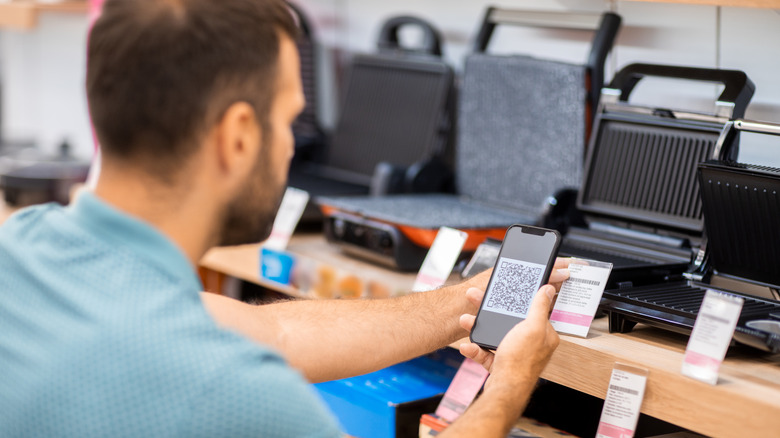 A young man seen in a kitchen appliances store looking at he QR code of a toaster