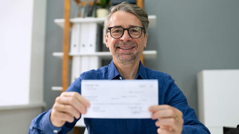 A smiling mature man holding up a check