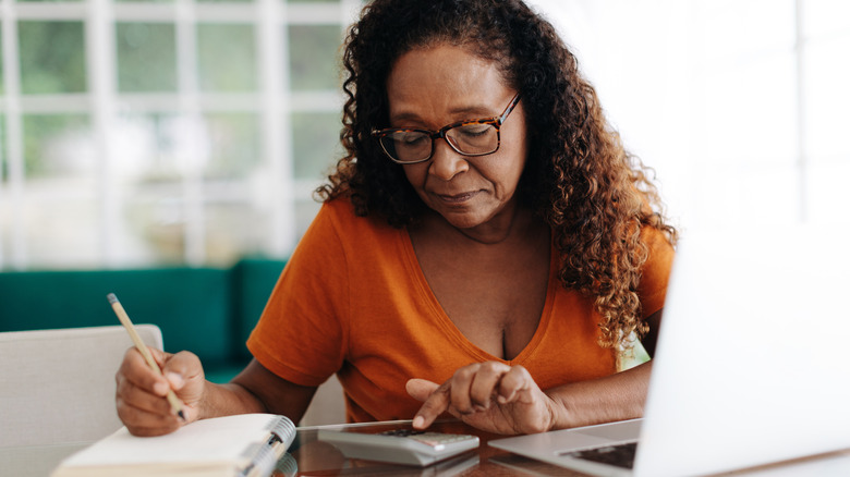 A mature woman using a calculator and writing on a notepad