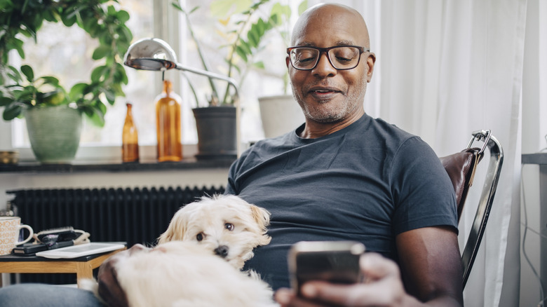 A middle-aged man with a dog in his lap looking at his cellphone