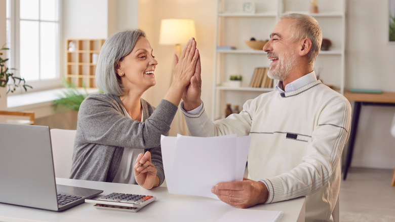 Senior citizen couple at a computer and high-fiving each other