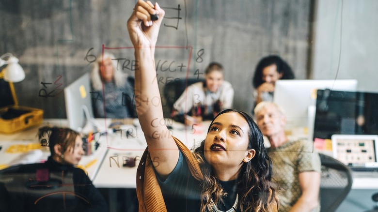 Person writes on transparent board during an office meeting