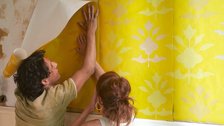 Two people putting up wallpaper