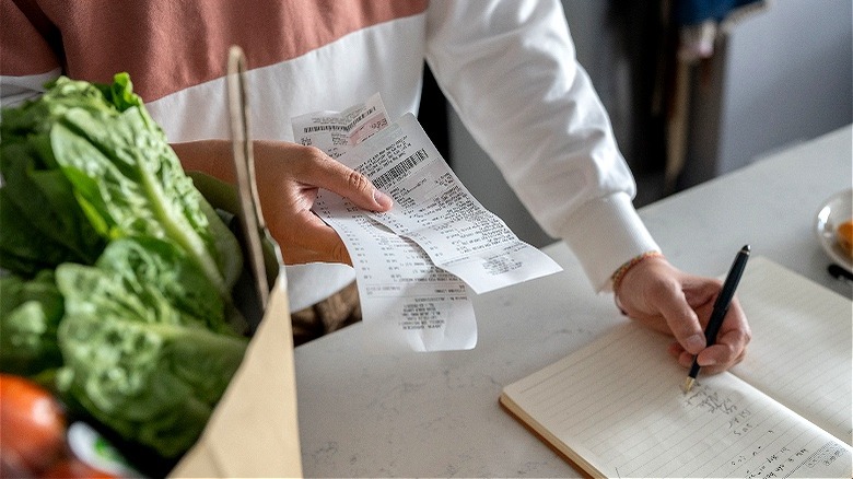 Person writing in grocery-price book