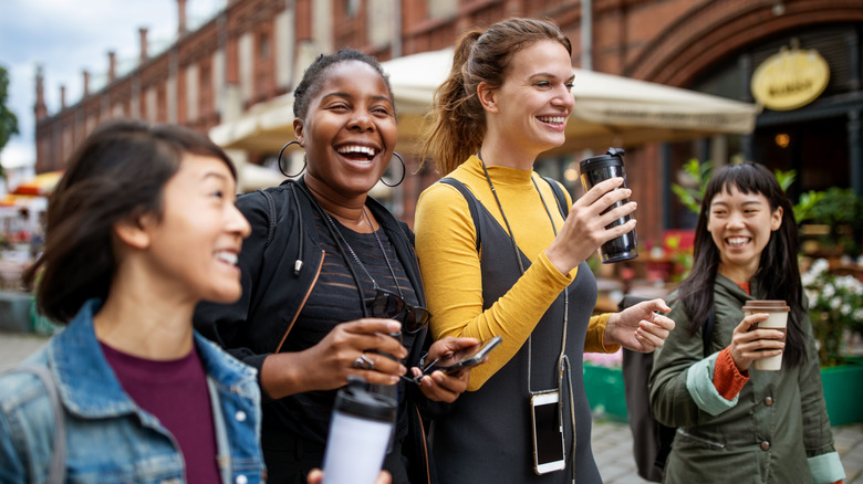 women walking on the street smiling while having a drink