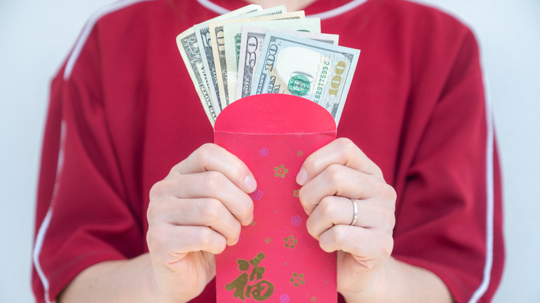 A person holding small red and gold packets containing money