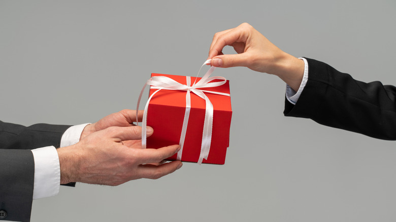 Closeup side view of hand holding out red gift box to another hand