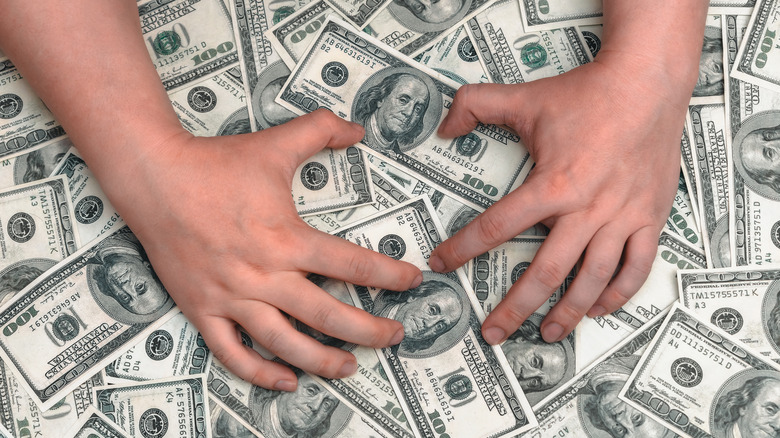 Hands lie on top of a huge pile of hundred-dollar bills