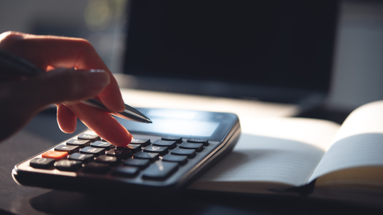 closeup of hand using calculator and holding pen