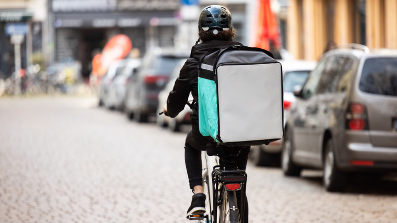 Rear view of a food delivery boy on a bike in city.