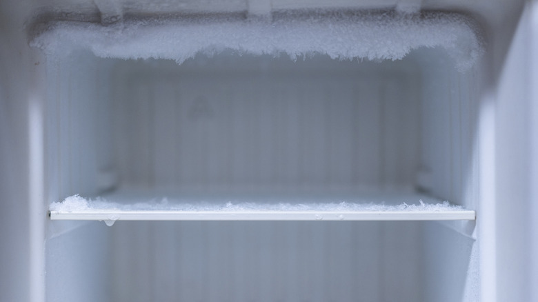 An empty and frosty fridge freezer, with snowy frost on the shelf.