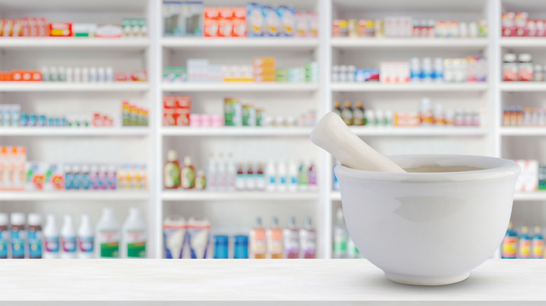 Mortar and pestle with full pharmacy shelves in background.