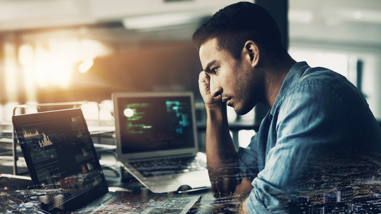 A depressed looking millennial man looking at a graph on a laptop screen