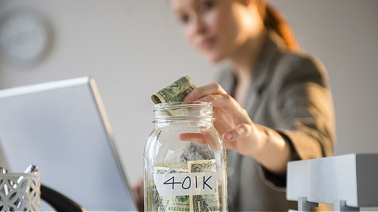 Close-up of a person's hand placing money into a 401K jar