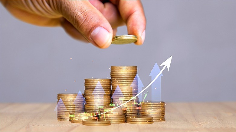 Hand seen stacking coins on coin stacks with upward arrow and stock chart overlaid