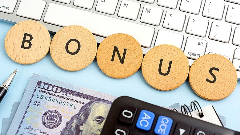 Desk with $100 bill, a keyboard, and the word 'BONUS' spelled out on wooden circles