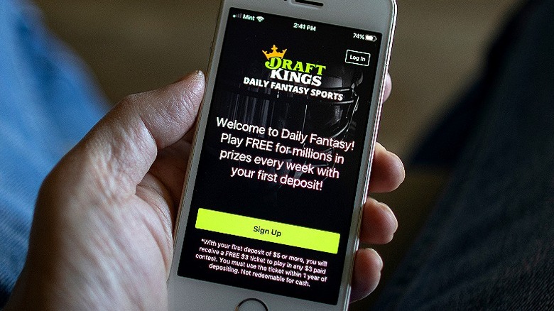 Hand holds phone displaying DraftKings sign-up screen