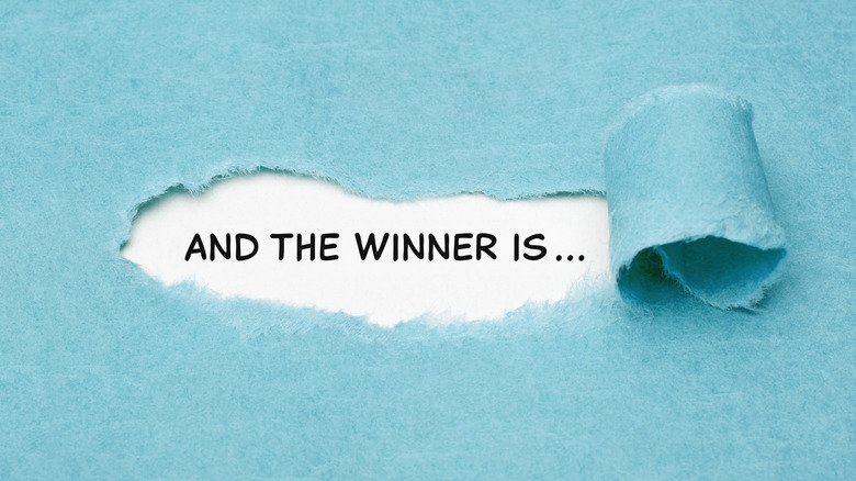 A blue piece of paper with a portion peeled back to reveal the words: And the winner is...