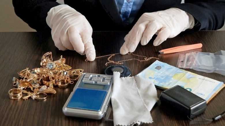 Someone with gloved hands assessing the value of several pieces of jewelry.