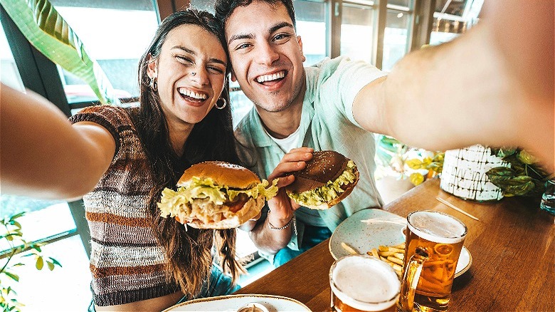 Two people smiling, holding burgers