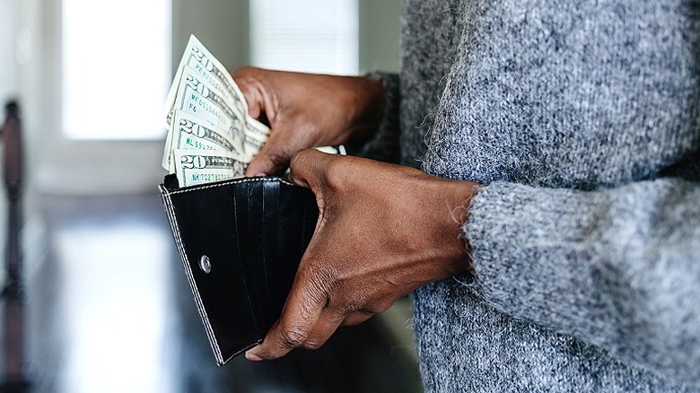 A close-up of a person's hands as they add $20 bills to a wallet