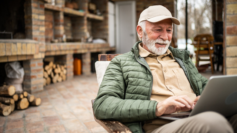 An elderly man sitting outside a cottage on a laptop