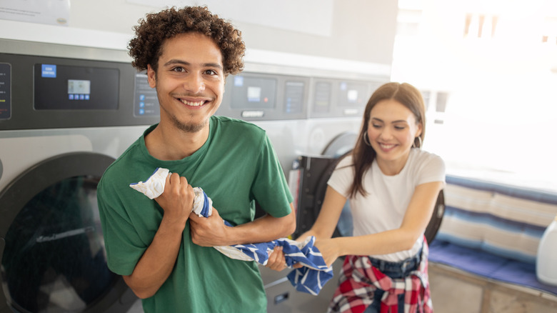 A gen z couple smiling while figting over a towel in a laundromat