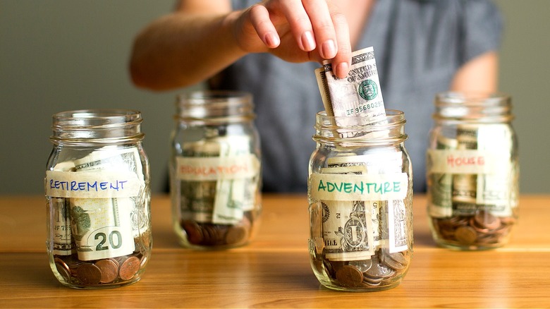 Multiple glass money jars seen labeled retirement, adventure, education, and house