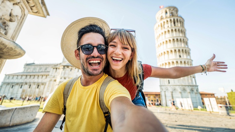 couple taking a selfie in front of the leaning Tower and Pisa cathedral