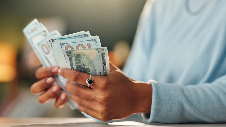 A close-up of a person's hands holding and counting several $100 bills