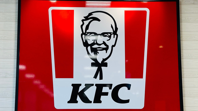 An illuminated red KFC restaurant sign, containing a white bucket-shaped logo and a vector illustration of Colonel Sanders.