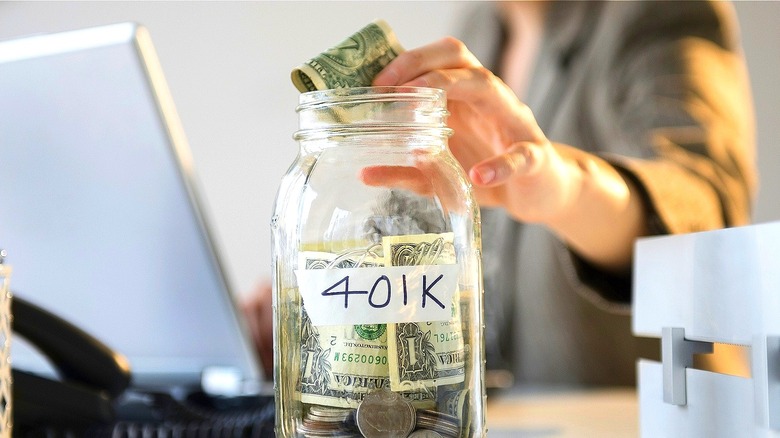 Person putting cash into glass jar marked 401K