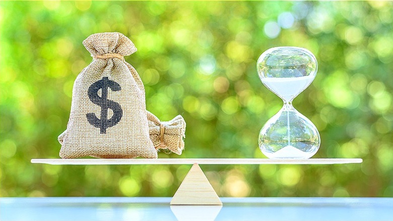 Money bag and hourglass balanced on seesaw on a table