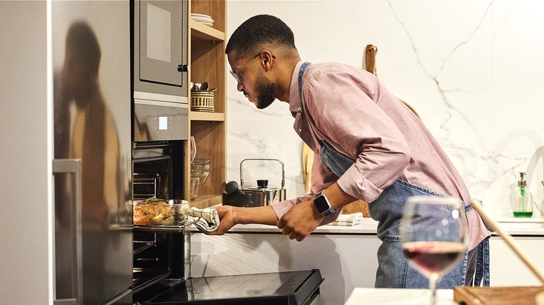 Man pulls dish from oven rack in home kitchen with wine glass on counter