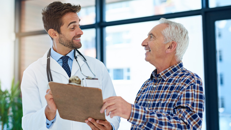 A senior man smiling at a doctor holding a clipboard.