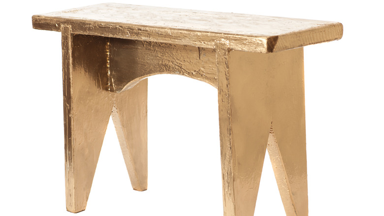 A solid gold stool with a white background