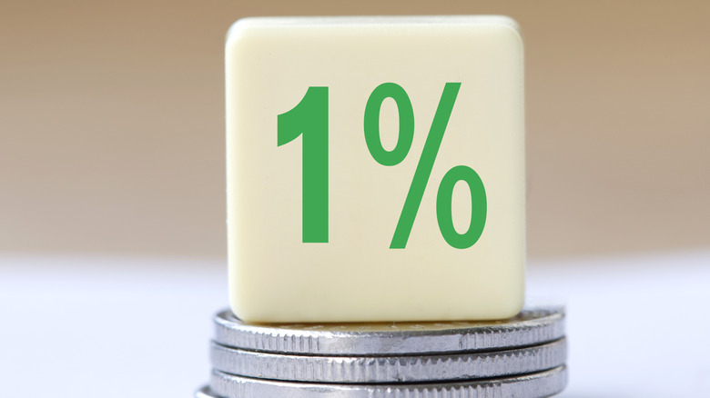 A square tile reading '1%' sitting on a stack of coins.