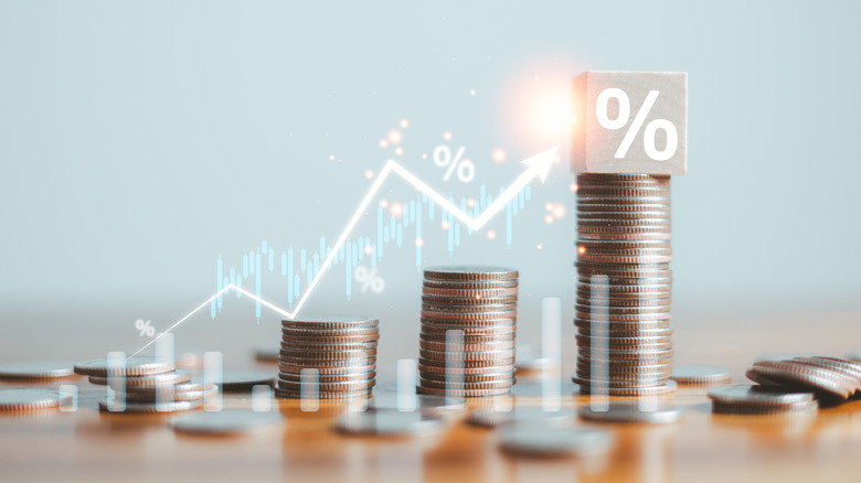 Graduating stacks of coins with a cube showing a percent sign sitting atop the tallest stack.