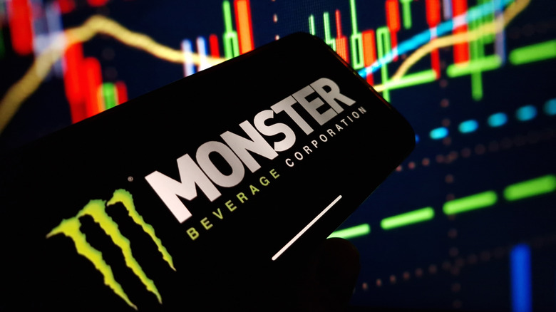 Monster Beverage logo on smart phone screen over stock charts