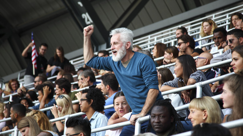 People of various ages watching what appears to be a sporting event from the bleachers.