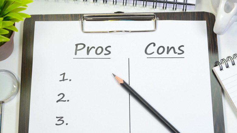 A clipboard holding a piece of paper with a column labeled 'Pros' on the left and 'Cons' on the right.