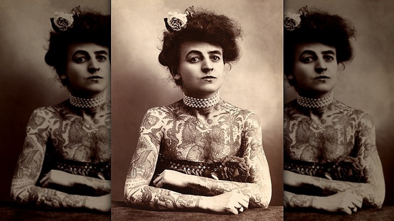 A sepia-toned photograph of an early circus tattooed lady, her neck wrapped in pearls and tattoos