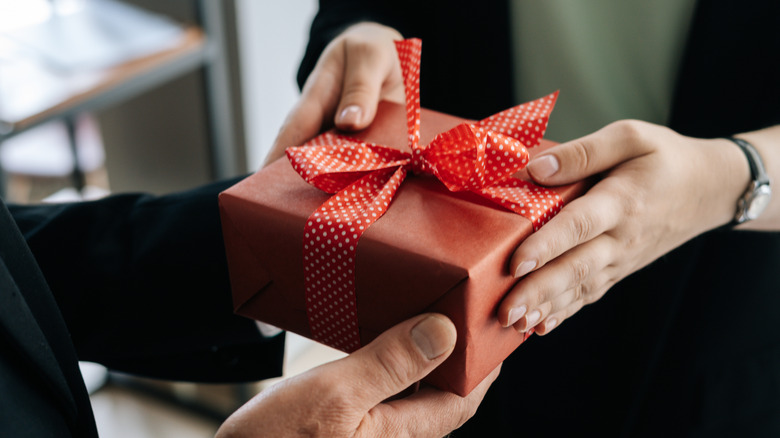 Close-up on hands and gift as an employee gives a gift to their boss in an office setting.