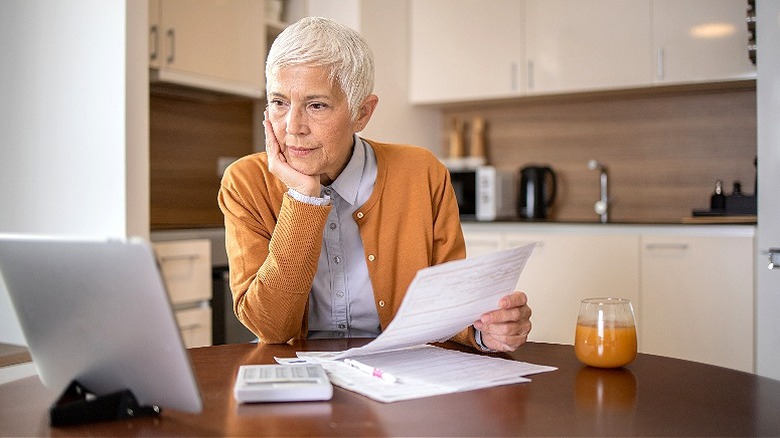 Older woman sitting in kitchen looking over paperwork and tablet