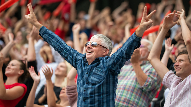 A excited senior man smiling while standing in a stadium crowd